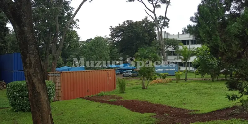 Before: NIA headquarters grounds before landscaping: rough grass, bare soil and a shipping container